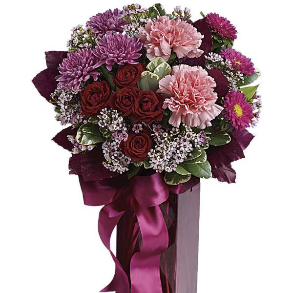 Bouquet of pink and red flowers in a tall glass vase with a ribbon
