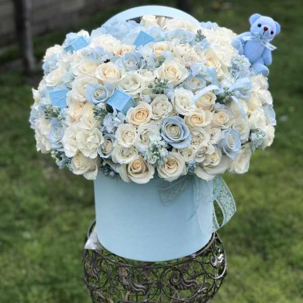 Blue and white rose arrangement in a round hatbox with a teddy bear
