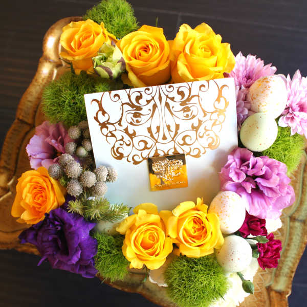 Floral gift arrangement with yellow roses, purple blooms, and decorative eggs in a tray