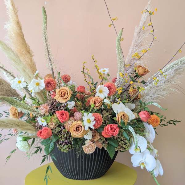 Large floral arrangement with peach roses, white orchids, and pampas grass in a black vase