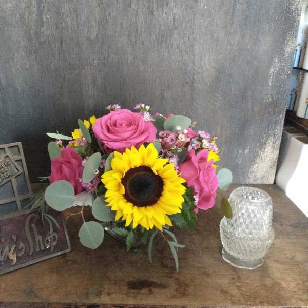 Pink roses and a sunflower in a low glass vase with small filler flowers