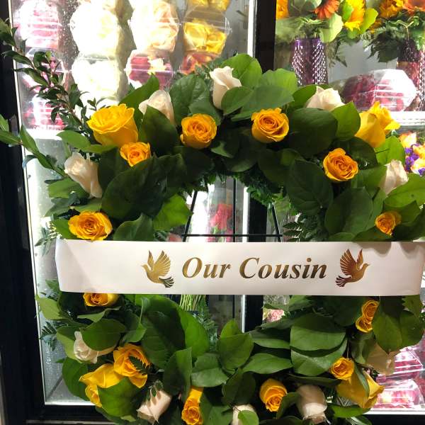 Yellow and white rose wreath on an easel with a memorial ribbon