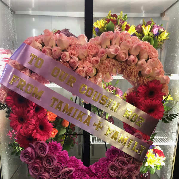 Heart-shaped floral wreath with pink roses and gerberas, with ribbon text