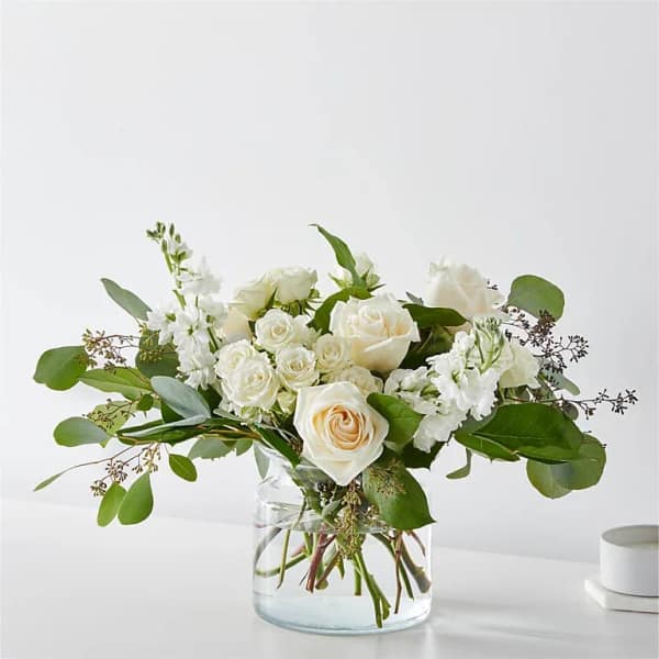 White roses and white blooms in a clear glass vase with greenery