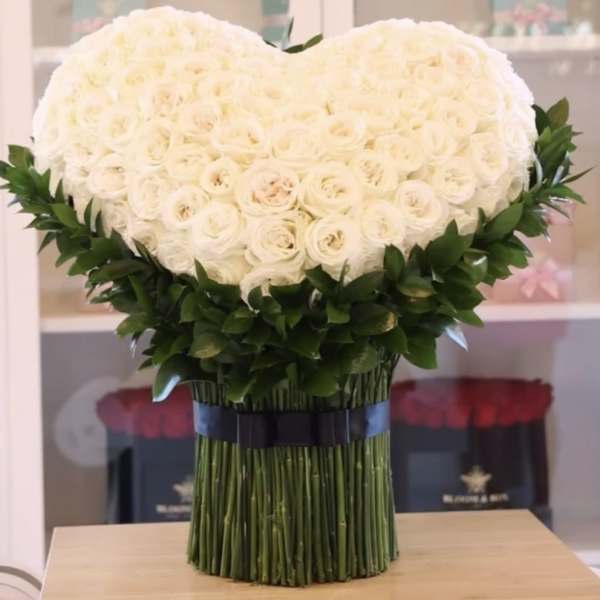 Heart-shaped bouquet of white roses with dark green foliage