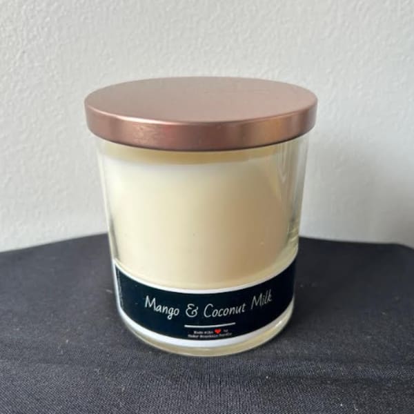 A mango and coconut milk candle in a glass jar with a metallic lid