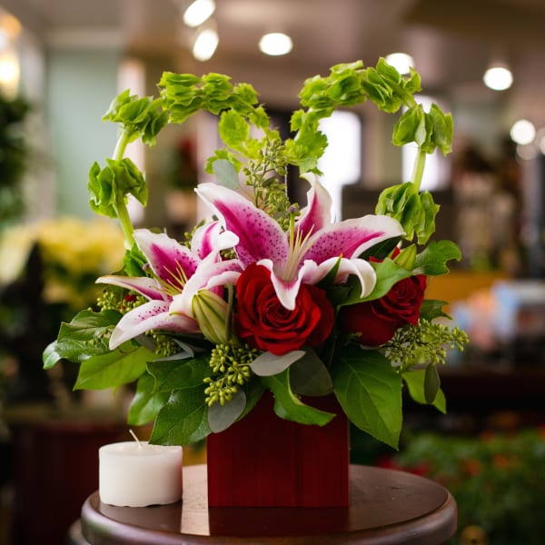 Red roses and pink lilies in a red square vase with a white candle