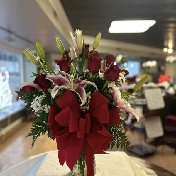 Red roses and lilies in a glass vase with a large red bow