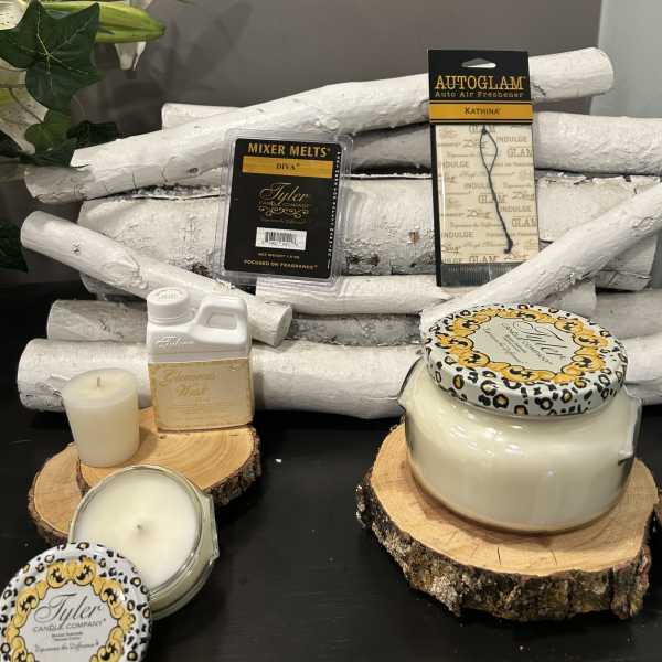 Candles and fragrance products arranged on wood slices with a few lily stems at left