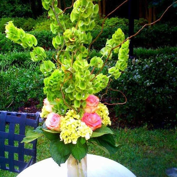 Tall floral arrangement with green orchids and pink roses in a glass vase