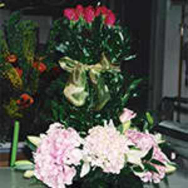 Tall green topiary with pink roses above pink blossoms and lilies, tied with a gold bow.