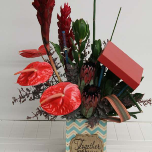 Tropical arrangement with red anthuriums, protea, and succulents in a patterned box with a red box accent.