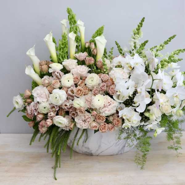 Low marble container filled with blush roses, white ranunculus, calla lilies, and cascading white orchids