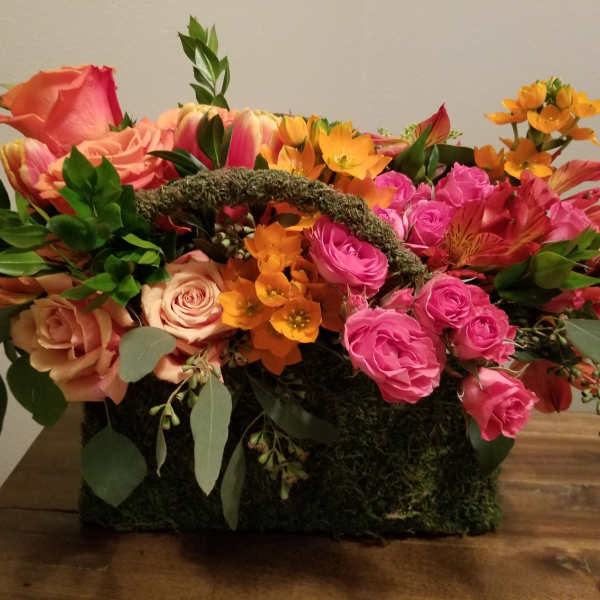 Mixed bouquet of pink and orange roses in a moss-covered basket