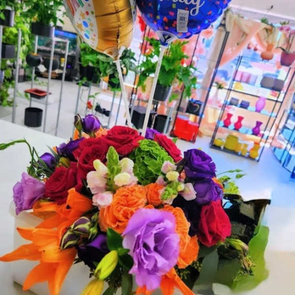 Colorful mixed flower arrangement with birthday balloons in a white rectangular container.