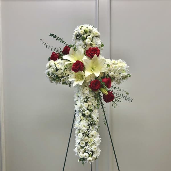 White floral cross on a stand with red roses and lilies