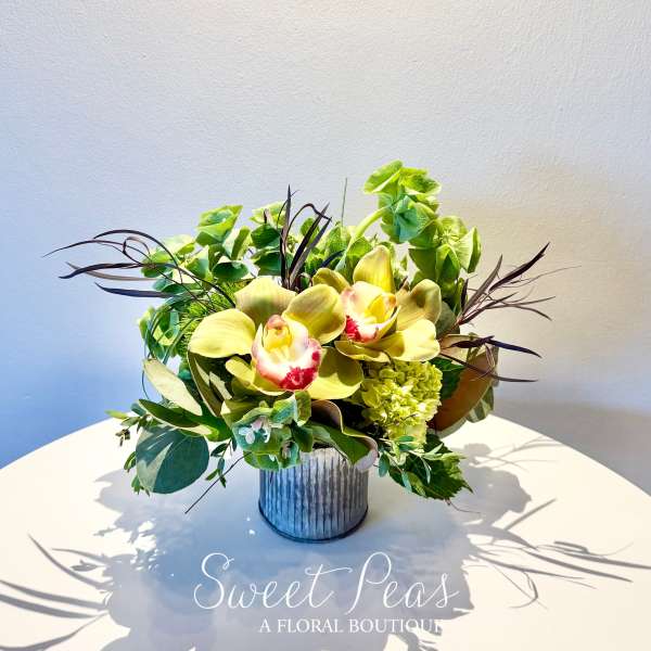 Low arrangement of green cymbidium orchids and hydrangea in a ribbed metal vase