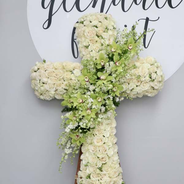 White rose cross-shaped floral tribute with green orchids on an easel