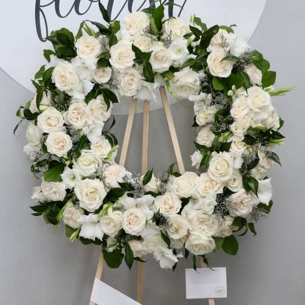 White rose wreath on a wooden easel with greenery