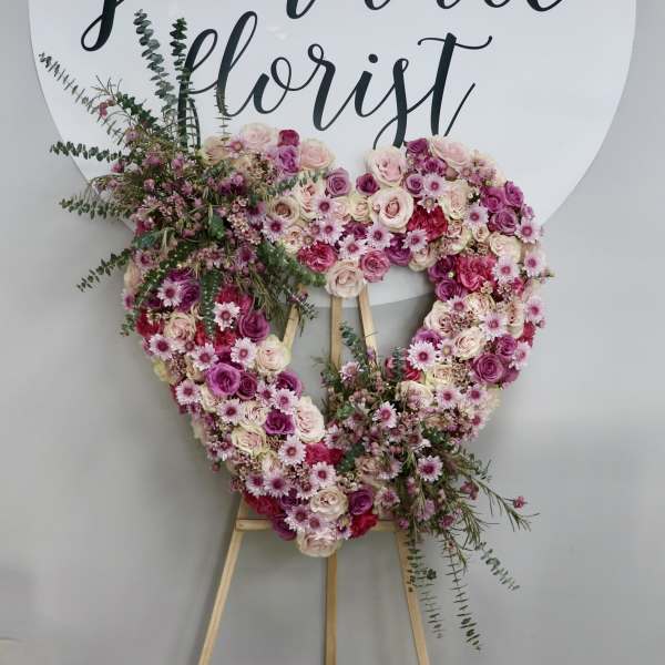 Heart-shaped floral wreath on an easel with pink and white roses