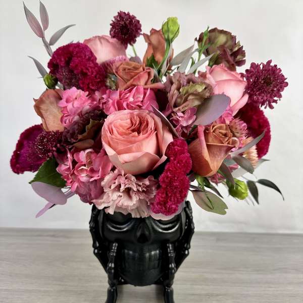 Pink and burgundy bouquet in a black skull vase