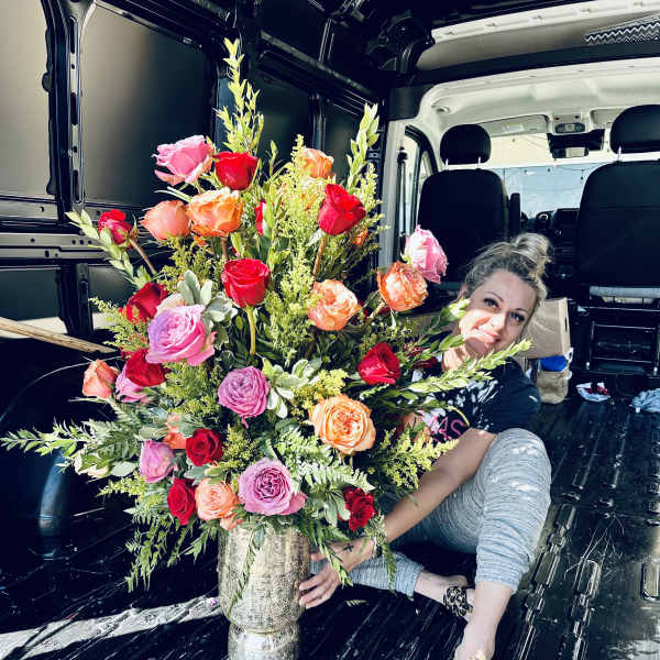 Large mixed rose arrangement in a silver vase with a woman beside it