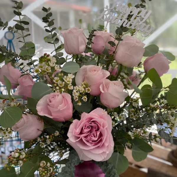 Pink rose birthday arrangement with filler flowers in a pink vase and a Happy Birthday pick.