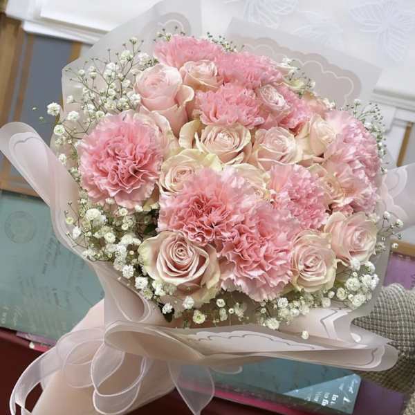 Pink roses and carnations in a wrapped bouquet with baby's breath