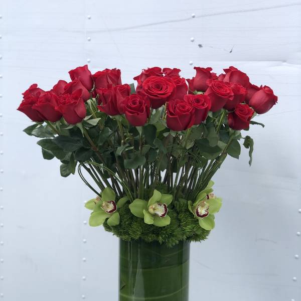 Red roses arranged in a tall green vase with green orchids at the base