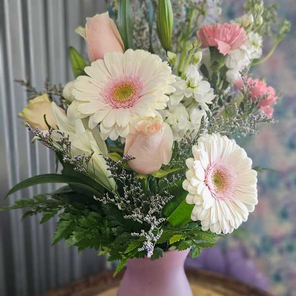 Pastel bouquet of gerbera daisies, roses, lilies, and carnations in a pink vase