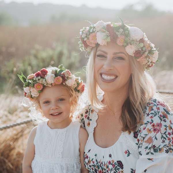 Woman and child wearing floral crowns and white dresses outdoors