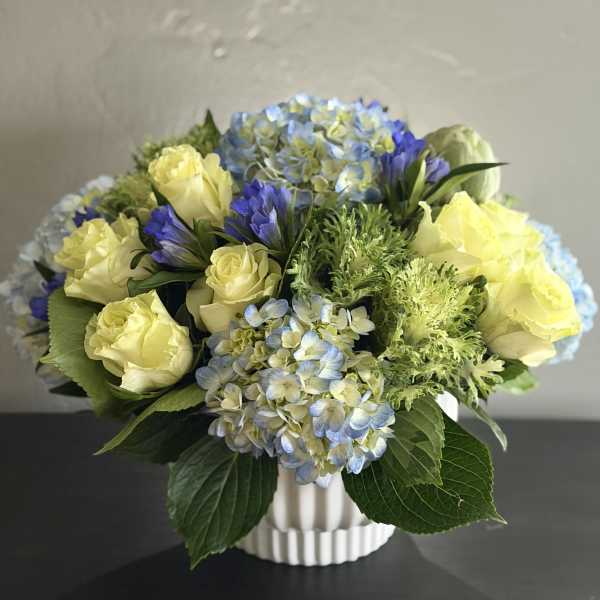 Yellow roses and blue hydrangeas in a white vase