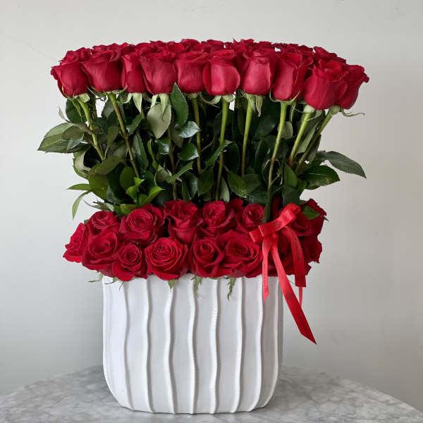 Two tiers of red roses in a white ribbed vase with a red ribbon