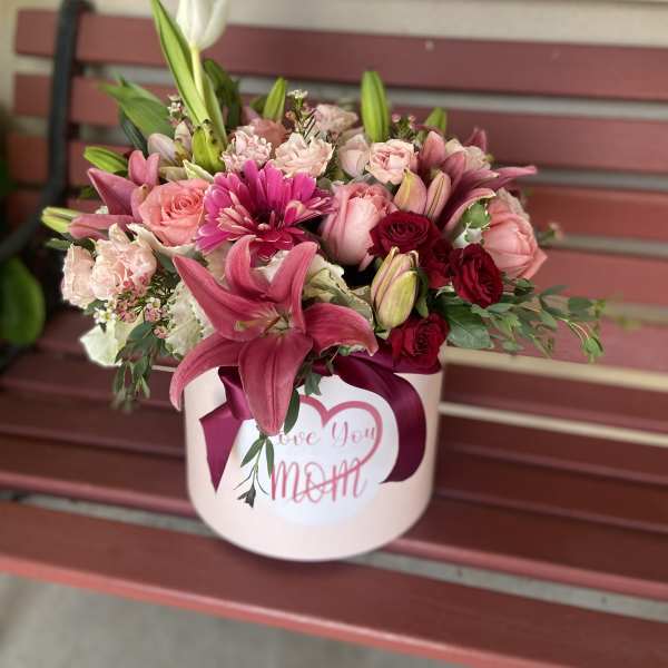 Pink and red mixed flower arrangement in a round box with a ribbon