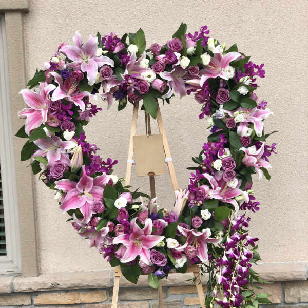 Heart-shaped floral wreath with pink lilies, purple roses, and orchids on an easel