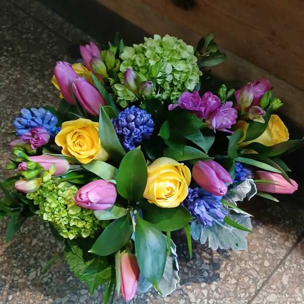 Compact bouquet of yellow roses, pink tulips, green hydrangeas and purple-blue hyacinths.