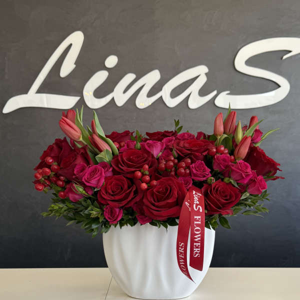 Red and pink rose arrangement in a white vase with lily buds