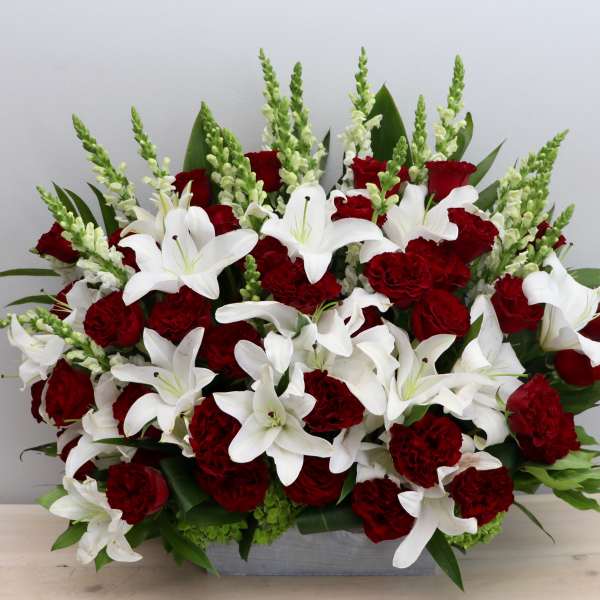 Red roses and carnations with white lilies and snapdragons in a low rectangular container