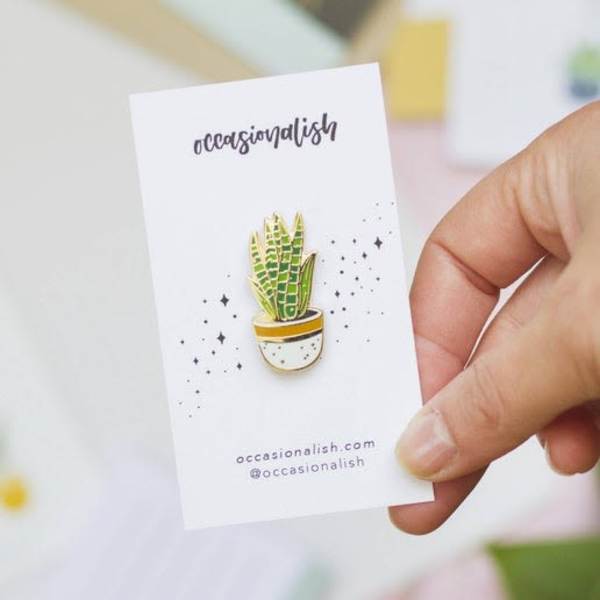 Hand holding a card with a small potted plant pin