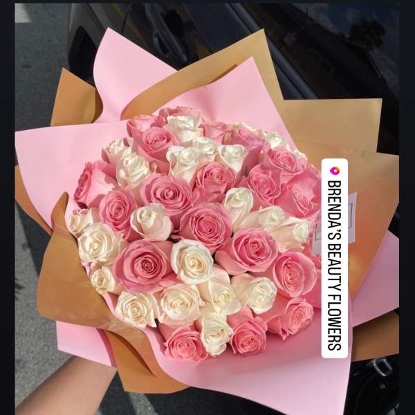 Hand-tied bouquet of pink and white roses wrapped in layered pink and tan paper