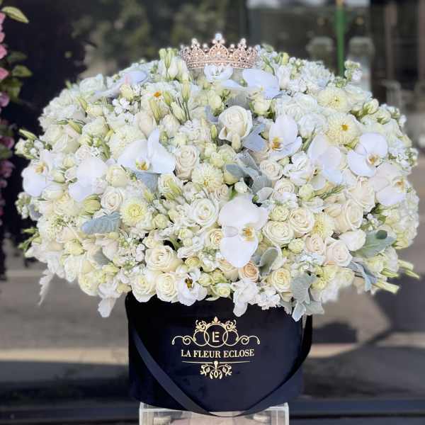 Large white floral arrangement in a black hat box with a tiara on top.