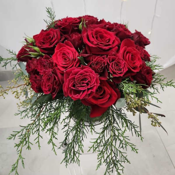 Compact arrangement of red roses in a glass vase with trailing evergreen accents
