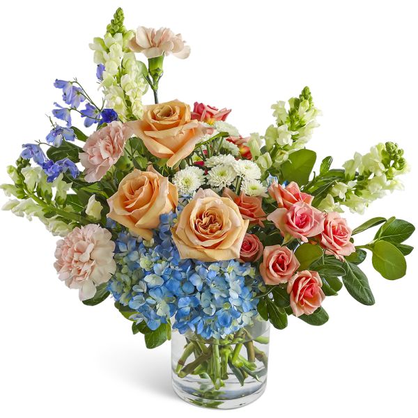 Mixed bouquet of peach roses, blue hydrangea, and assorted blooms in a clear glass vase