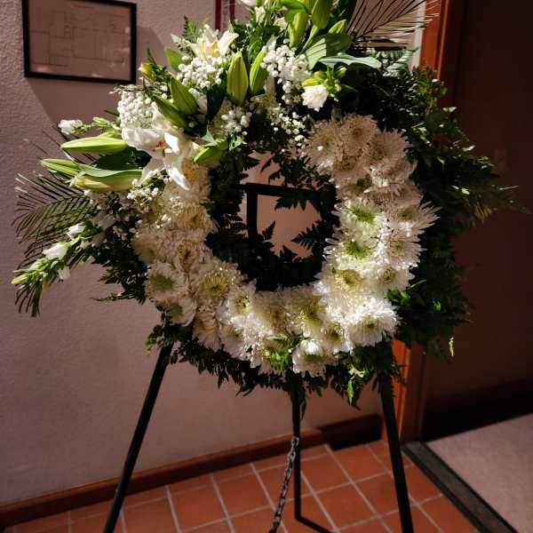 White floral wreath on a black easel with lilies and daisies
