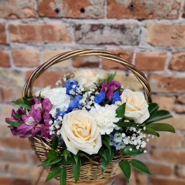 Basket arrangement with cream roses, purple blooms, and blue flowers