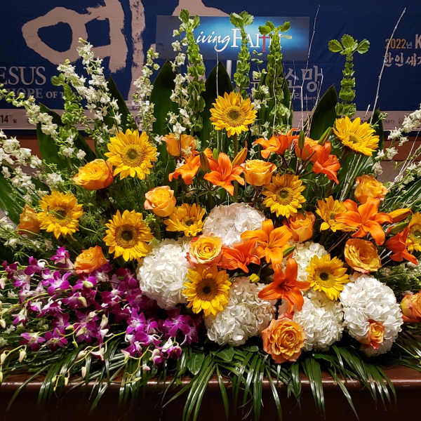 Large altar arrangement of orange lilies, yellow blooms, white hydrangeas, and purple orchids