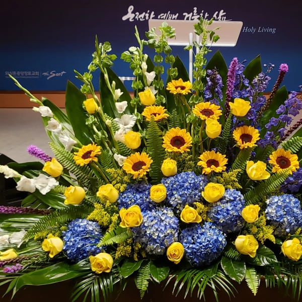 Large altar arrangement of yellow roses, sunflowers, blue hydrangeas, and tall purple accents