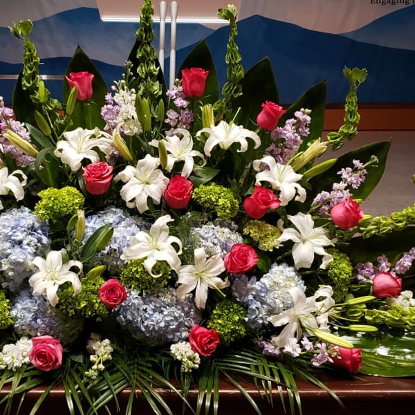 Large altar arrangement with white lilies, pink roses, blue hydrangeas, and green accents