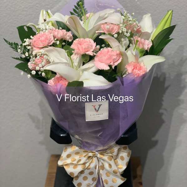 Hand-tied bouquet of white lilies and pink carnations wrapped in purple paper with a polka dot bow.