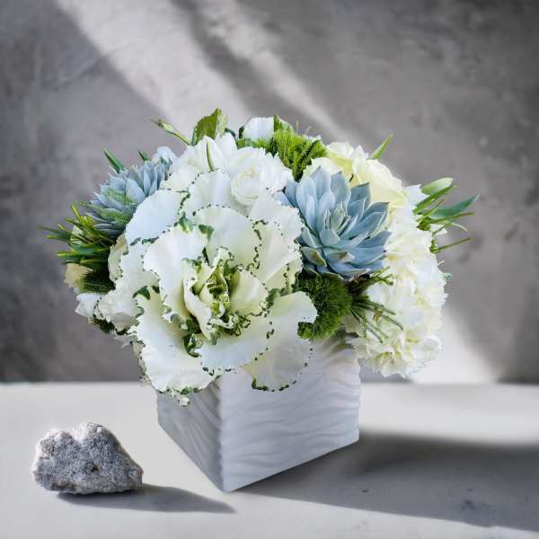 White and pale blue floral arrangement in a white square vase